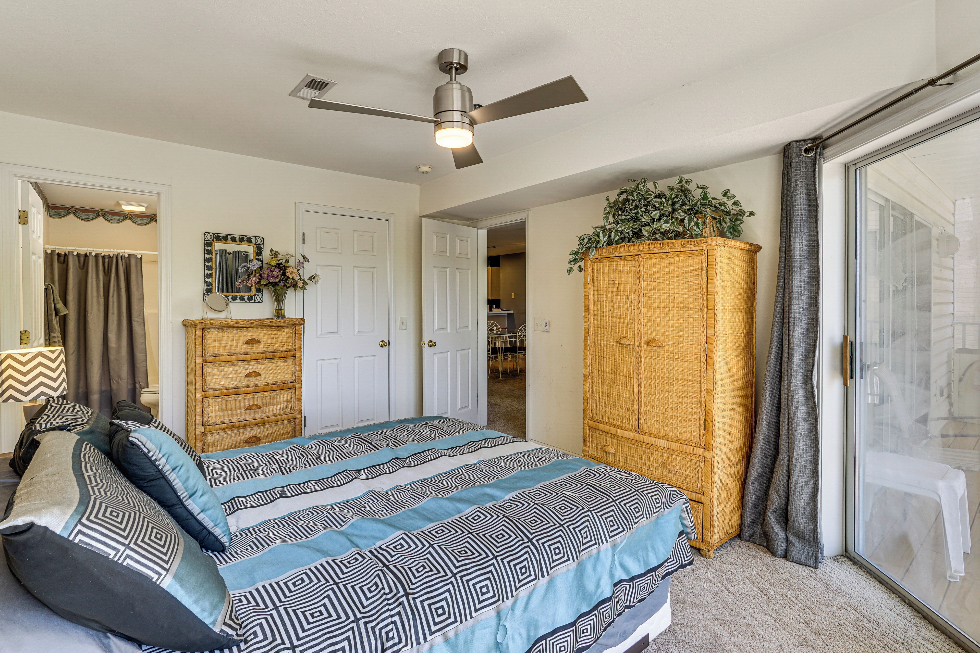 Une chambre à coucher comprenant un lit, un ventilateur de plafond, une armoire et une porte-fenêtre coulissante.
