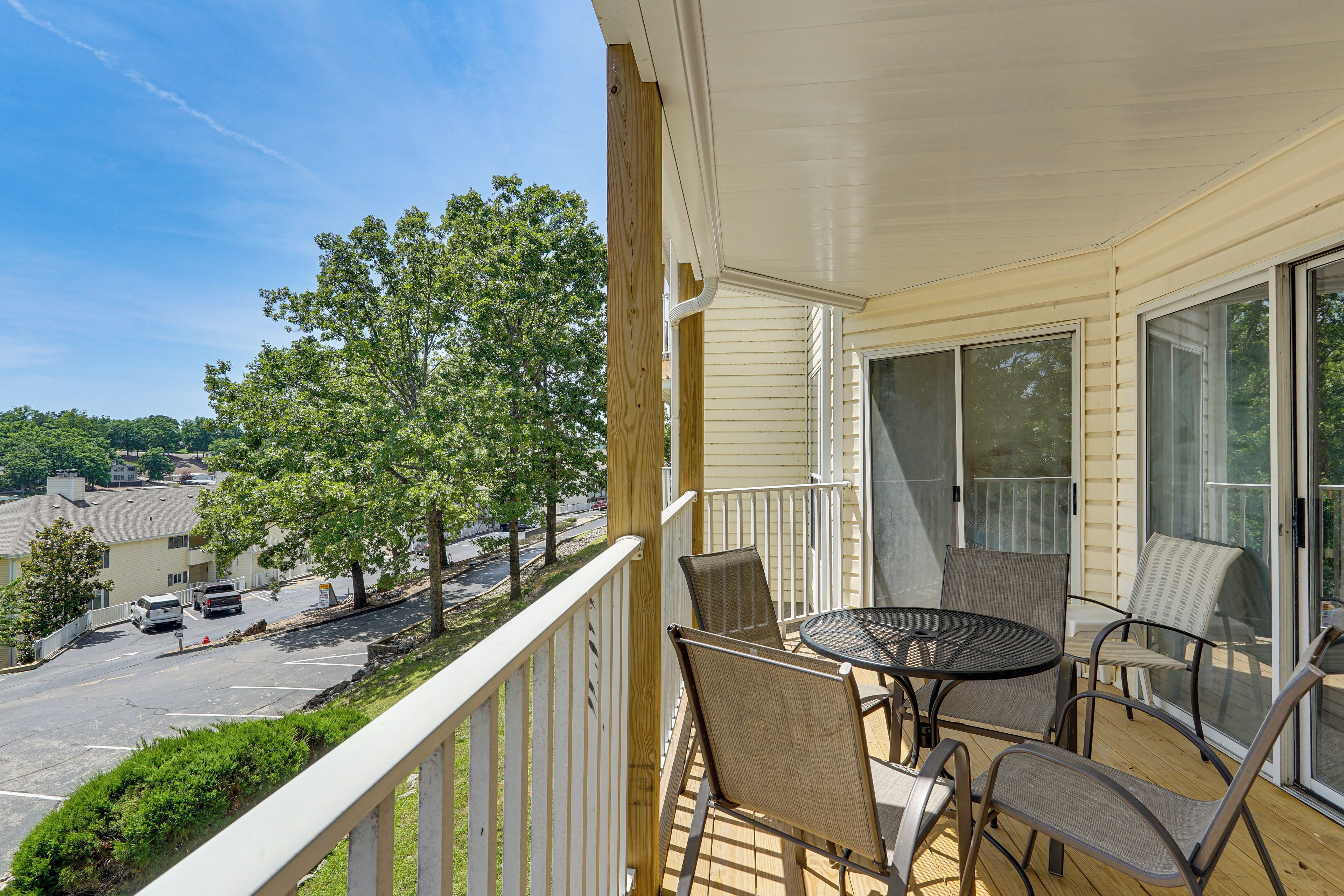 A balcony with a table and chairs, a view of a parking lot, and a tree.