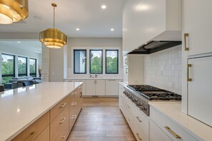 A modern kitchen with a large island, white cabinetry, and a gas stove. - Luxe Plymouth Group Getaway w/ Office & Foosball (Plymouth)