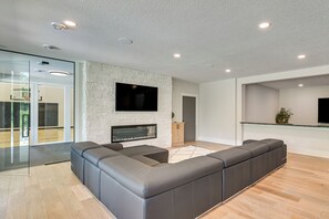 A modern living room with a sectional sofa, a fireplace, and a flat-screen TV mounted on a stone wall. - Luxe Plymouth Group Getaway w/ Office & Foosball (Plymouth)