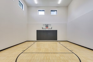 A basketball court with a hoop, two windows, and a wooden floor. - Luxe Plymouth Group Getaway w/ Office & Foosball (Plymouth)