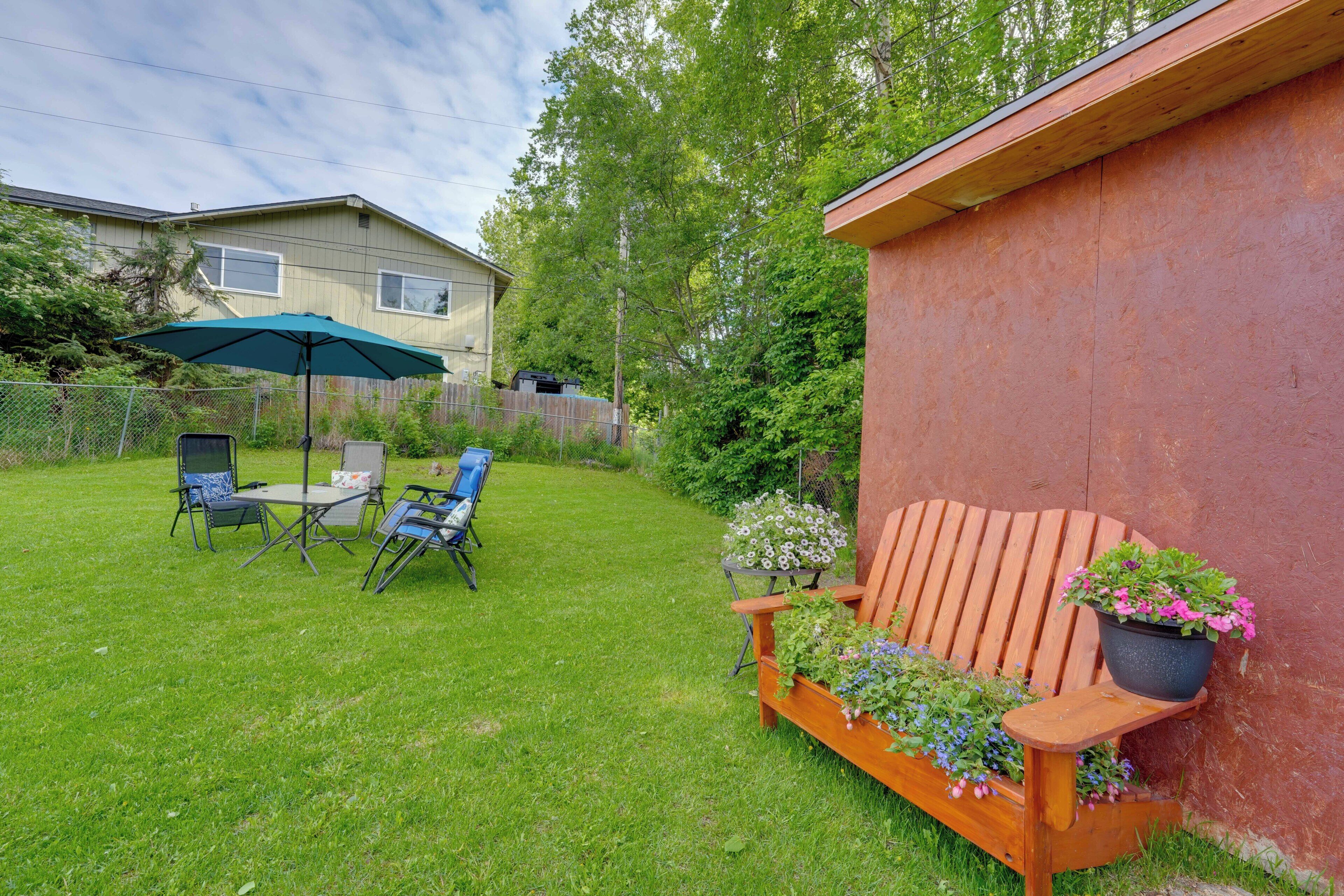A backyard with a wooden bench, a table with chairs, and a blue umbrella.