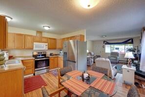 A kitchen with wooden cabinets, a microwave, a refrigerator, and a dining area with a glass table and chairs. - Family Friendly! Anchorage Haven w/ Private Yard (Anchorage)