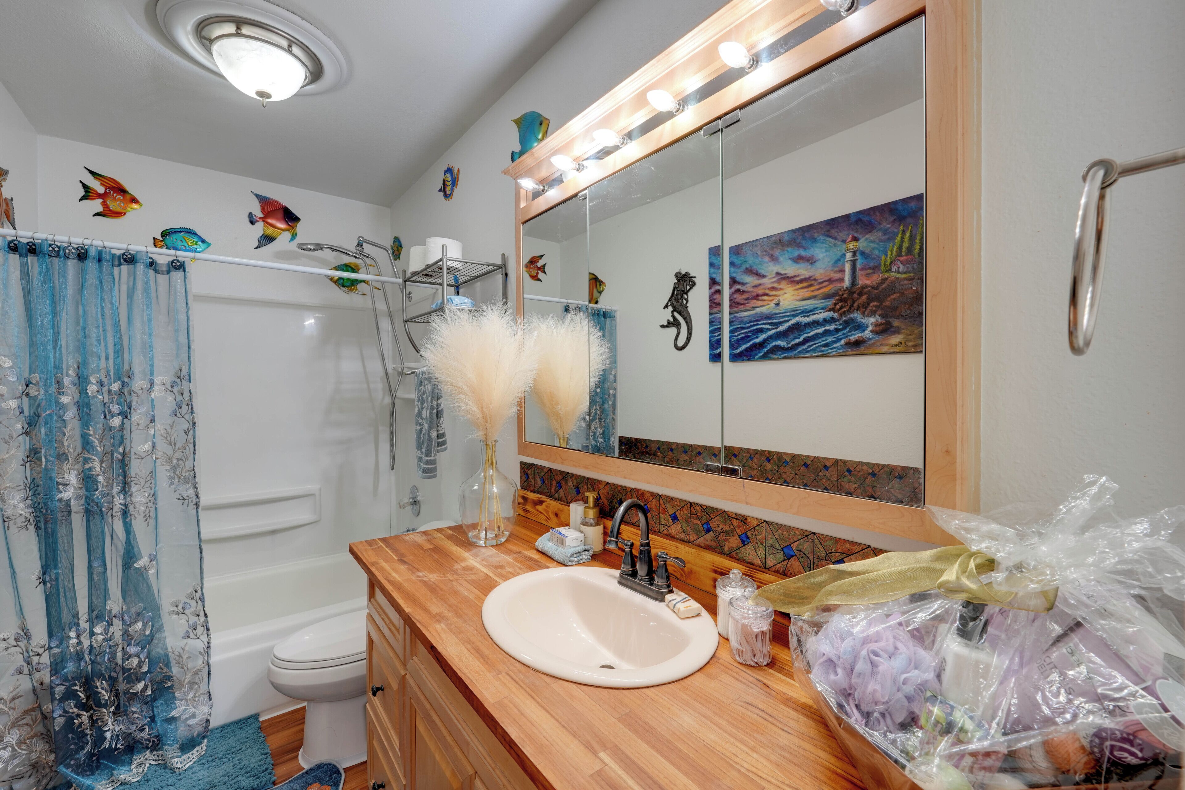 A bathroom with a wooden vanity, a sink, a mirror, a shower curtain, and a painting on the wall.