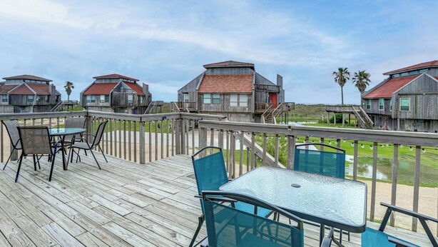 A wooden deck with outdoor seating and a view of beach houses.
