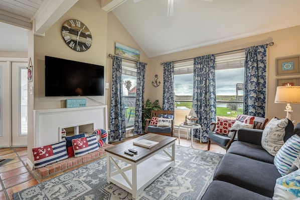 A living room with a fireplace, a television, and a view of the outdoors. - Walk to Matagorda Beach! Condo w/ Pool Access (Matagorda)