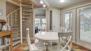 A dining area with a round table, white chairs, a staircase, and a view through a glass door.