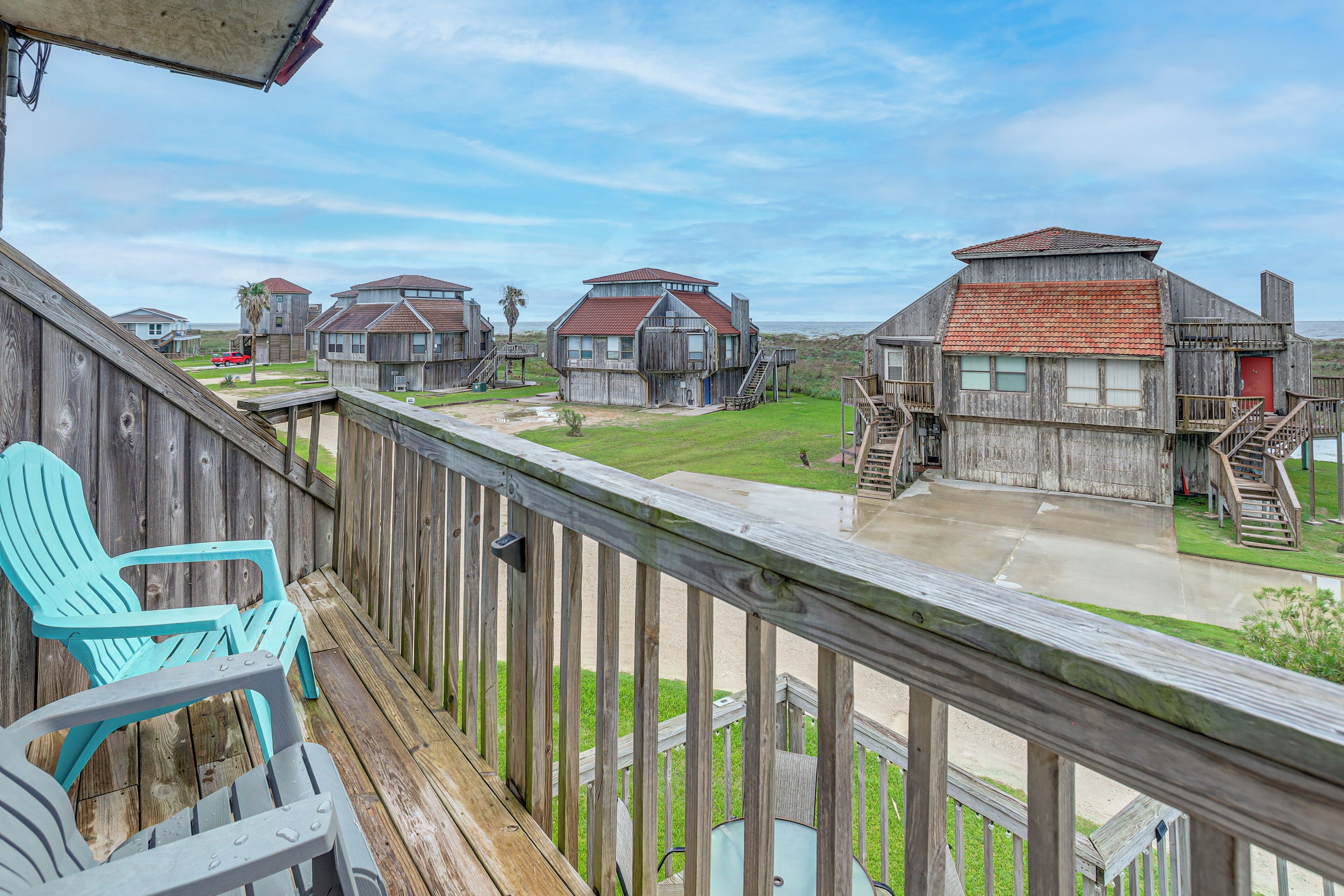 A wooden deck with chairs, a view of beach houses, and a clear sky.