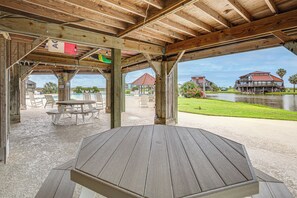 Un espace extérieur abrité, doté de tables de pique-nique et offrant une vue sur un lac et des bâtiments.
