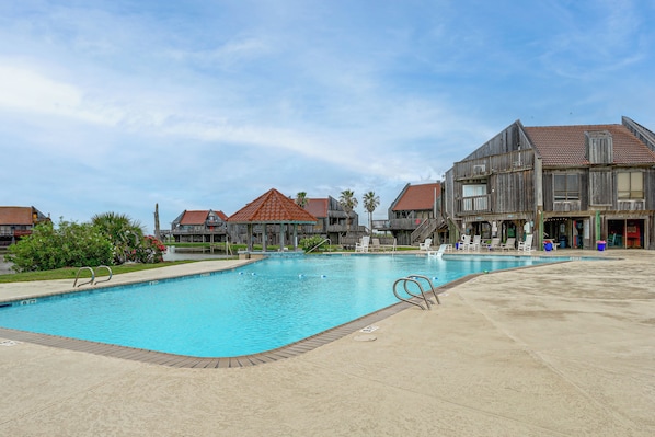 A swimming pool with lounge chairs and a wooden building with a red roof. - Walk to Matagorda Beach! Condo w/ Pool Access (Matagorda)
