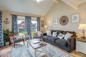 A living room with a sofa, armchair, coffee table, and a view of a house through the window. - Walk to Matagorda Beach! Condo w/ Pool Access (Matagorda)