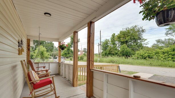 A porch with wooden rocking chairs, a hanging plant, and a view of a road and greenery.