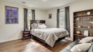 A bedroom with a bed, a nightstand, a dresser, a bookshelf, and a window with curtains.