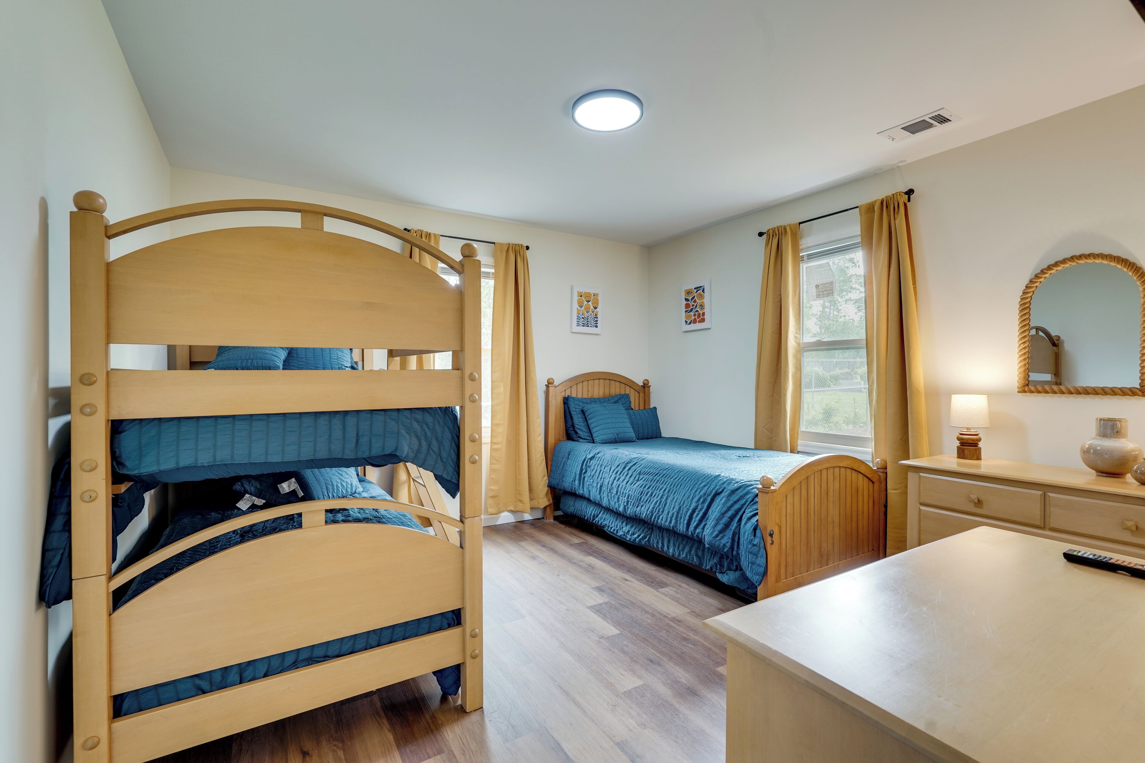 A bedroom with a bunk bed, a single bed, a dresser, a mirror, and a window with curtains.