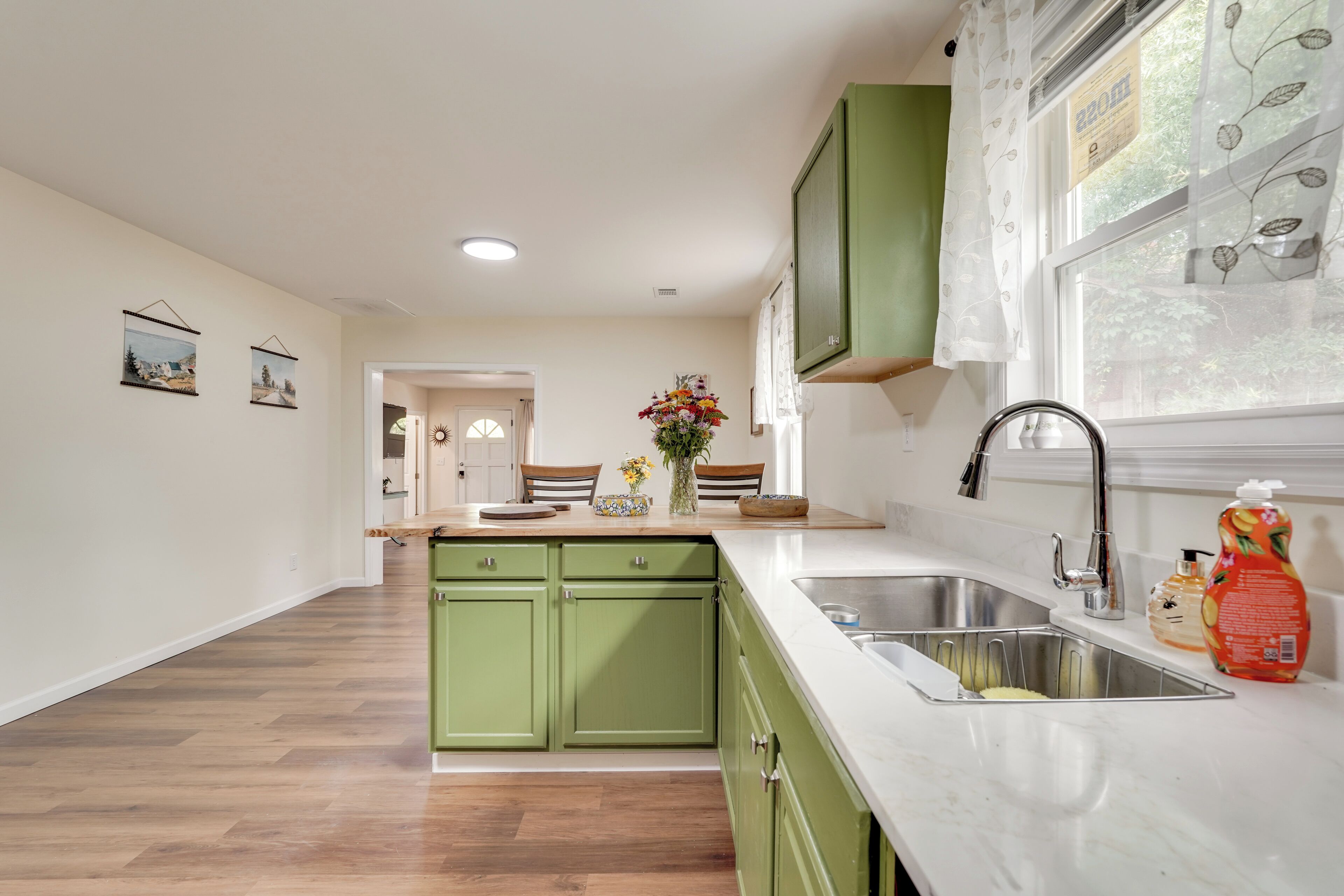 A kitchen with green cabinets, a white countertop, and a sink.