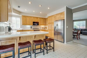 A modern kitchen with wooden cabinets, a stainless steel refrigerator, and a large island with stools.