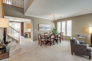A spacious living area with a dining table, chairs, a sofa, and a staircase leading to another level.