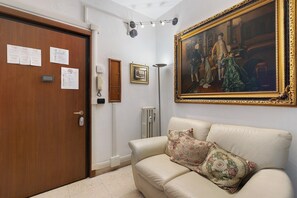 A room with a wooden door, a white wall, a framed painting, a radiator, a floor lamp, and a beige sofa with floral cushions. - 'Romaamor Casavacanze' Apartment with Private Terrace, Wi-Fi and Air Conditioning (Rome)