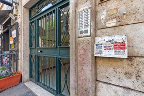 A building entrance with a green metal gate, a wall with various signs, and a potted plant. - 'Romaamor Casavacanze' Apartment with Private Terrace, Wi-Fi and Air Conditioning (Rome)