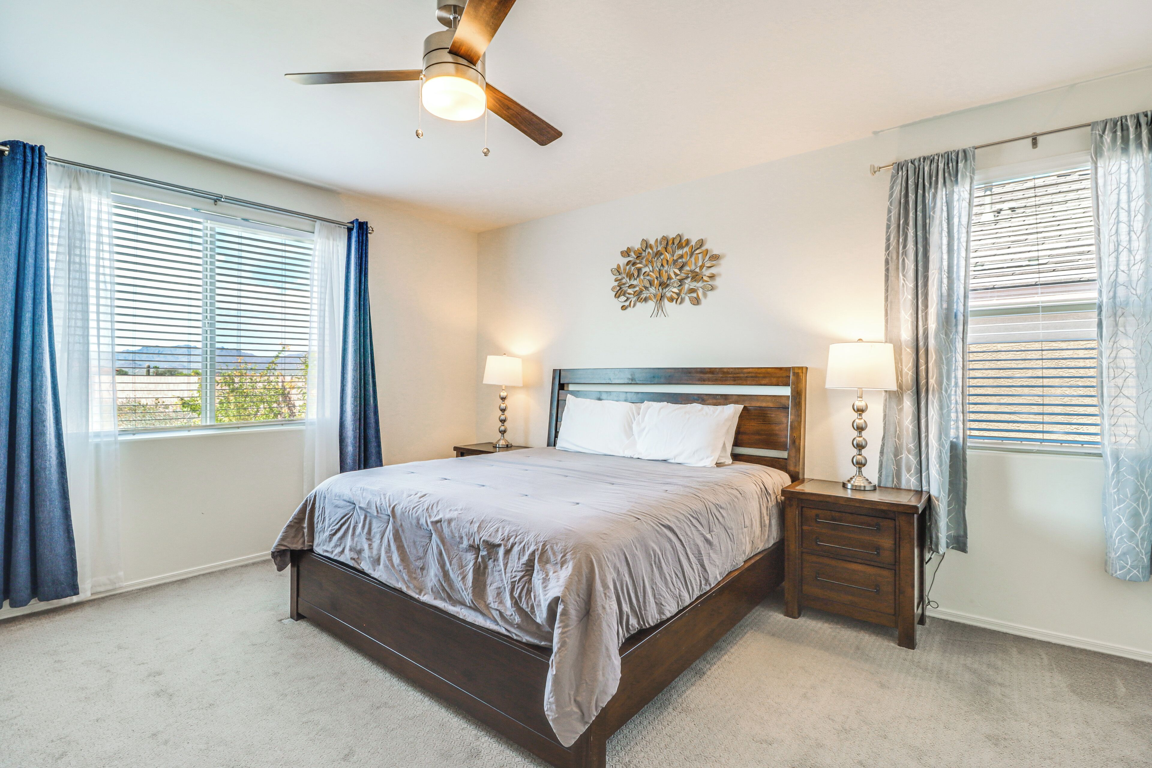 A bedroom with a bed, bedside tables, a ceiling fan, and a wall decoration.