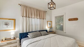 A bedroom with a bed, bedside tables, a lamp, a window with blinds, and a wall-mounted light fixture.