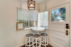 A corner with a white door, a window with blinds, a small white table, and three stools.