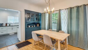 A dining area with a wooden table and chairs, a blue cabinet with glass doors, and a window with curtains.