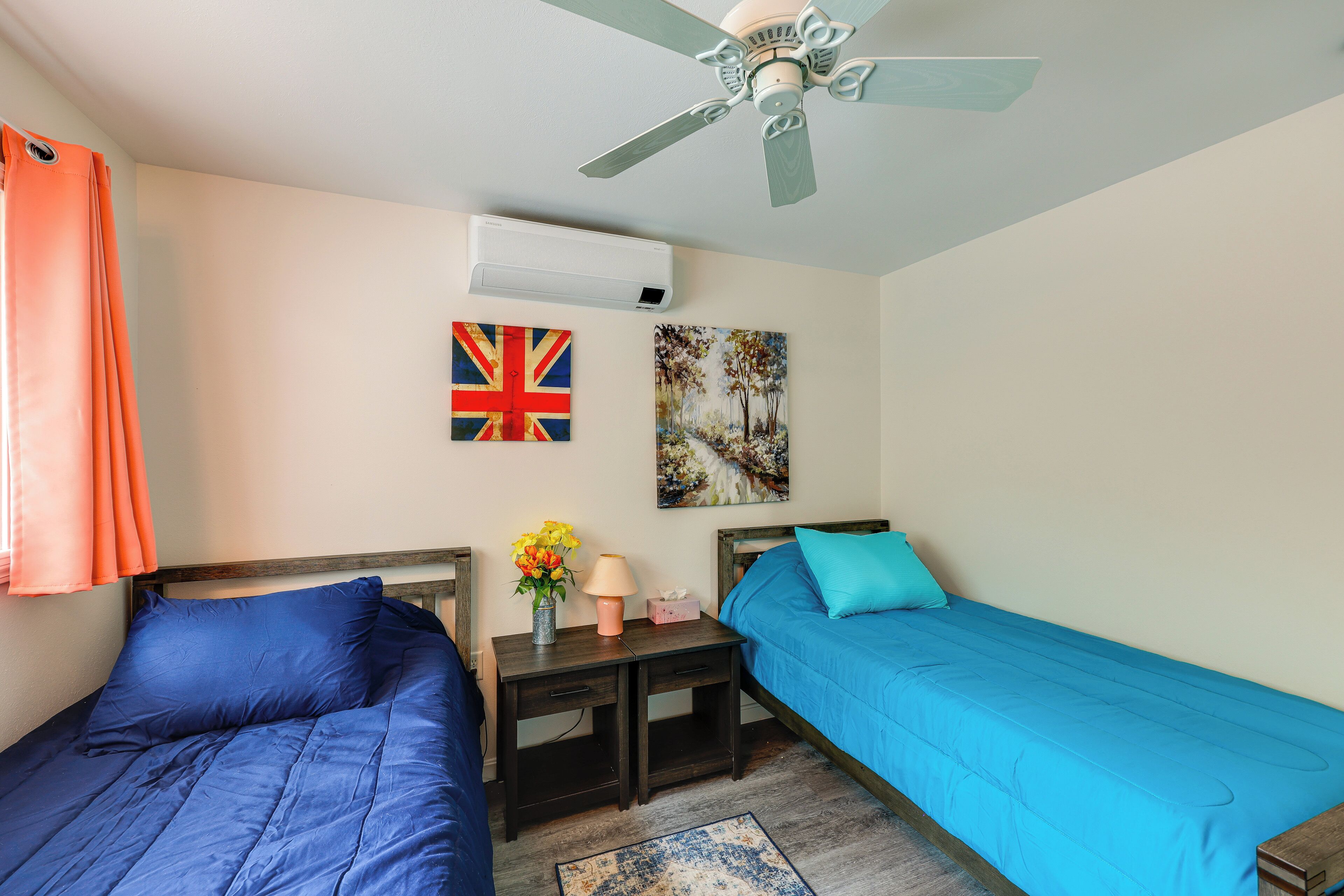 Une chambre avec deux lits, un ventilateur de plafond, un climatiseur et deux éléments de décoration murale.