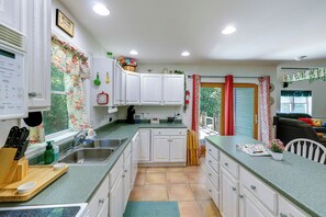 Una cocina con armarios blancos, encimera verde y una ventana con cortina floral.