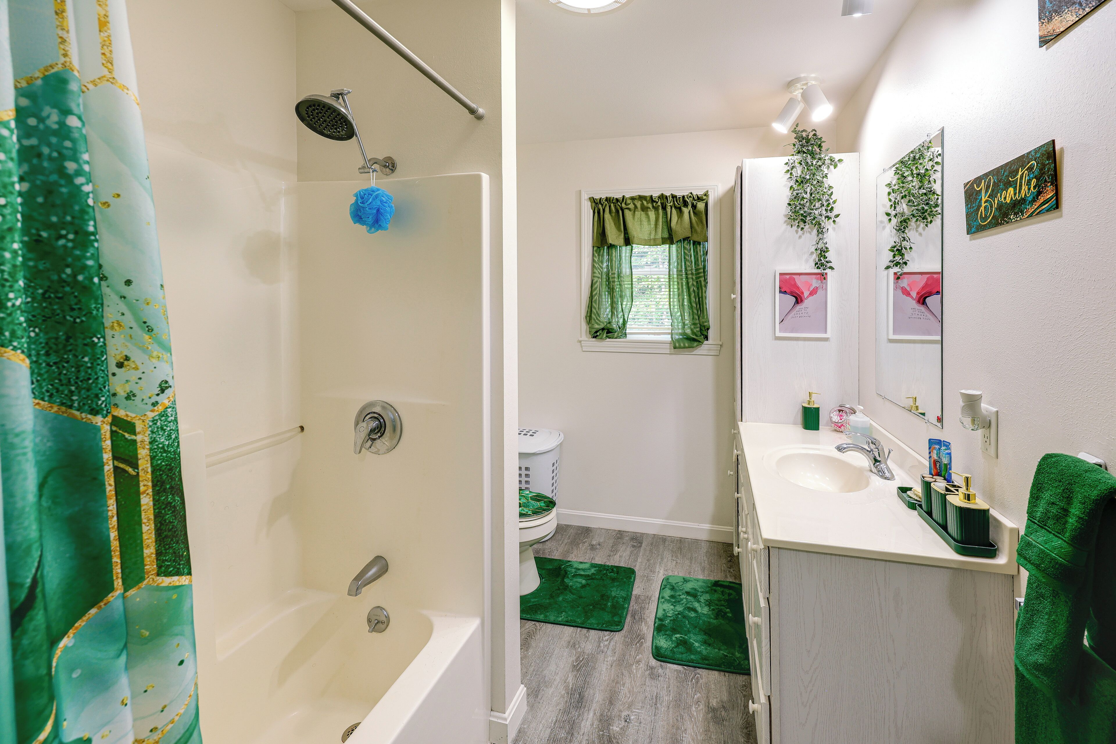 A bathroom with a bathtub, shower, sink, and green mats on the floor.