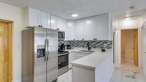 A modern kitchen with white cabinets, stainless steel appliances, a tiled backsplash, and a marble floor. - Close to Hard Rock Stadium! Group Getaway w/ Yard (Miami Gardens)