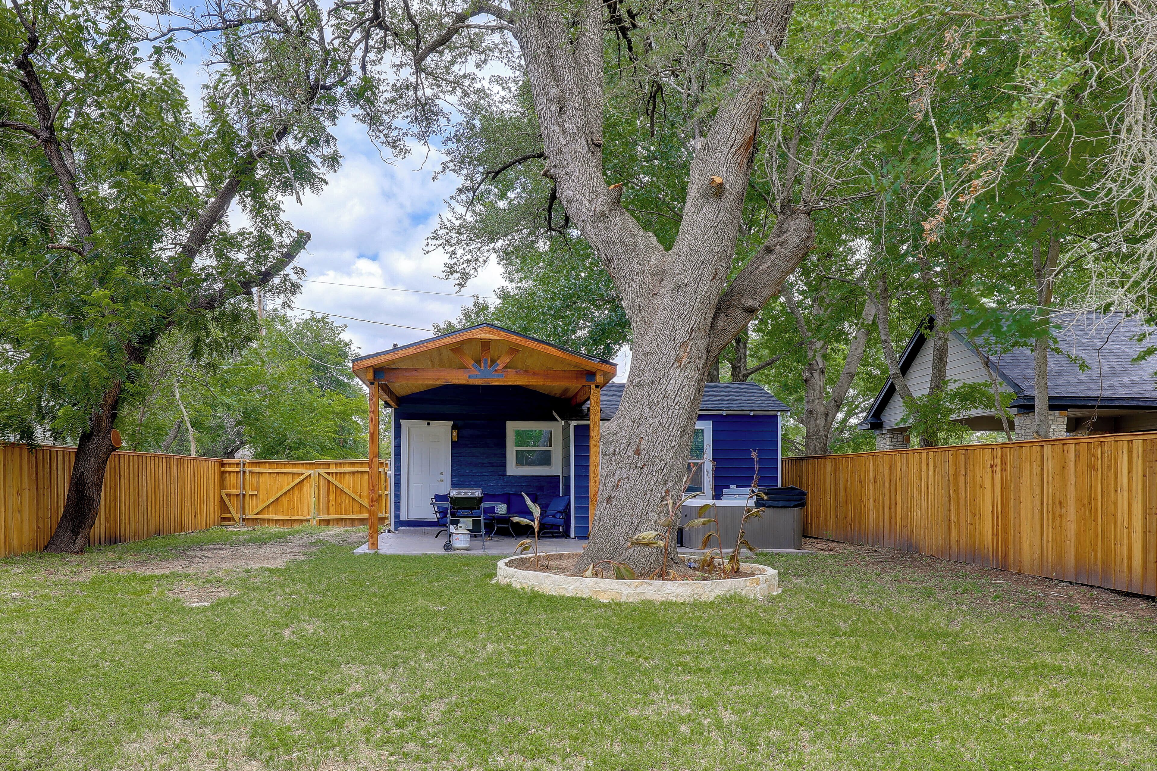 Un espacio al aire libre techado, con estructura de madera, un árbol y un patio cercado.