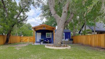 Un espacio al aire libre techado, con estructura de madera, un árbol y un patio cercado.
