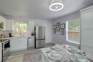 Una cocina moderna con armarios blancos, electrodomésticos de acero inoxidable y un comedor con vajilla blanca.