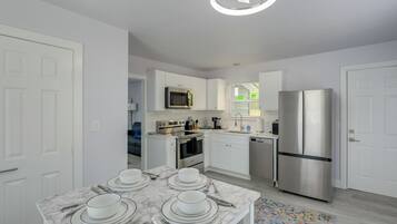 Una cocina moderna con armarios blancos, un refrigerador de acero inoxidable y un comedor con una mesa de mármol dispuesta para cuatro.