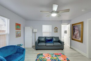 A living room with a grey sofa, a blue armchair, a ceiling fan, and a colorful rug. - Hot Tub, 1 Block to Granbury Square! Chic Studio (Granbury)