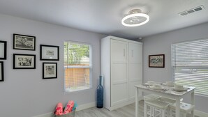 Une pièce comprenant une table à manger, des chaises, un meuble blanc, des tableaux encadrés accrochés au mur et une fenêtre avec des stores.