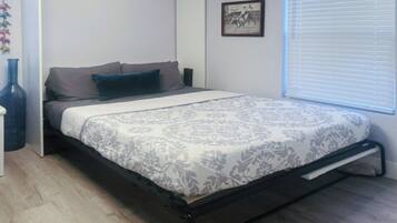 A bedroom with a bed, a nightstand, a wall-mounted picture, and a window with blinds.