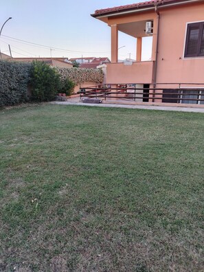 A grassy area with a fence, a building with a tiled roof, and a wall with a climbing plant. - Lola House Between Alghero and Stintino (Palmadula)