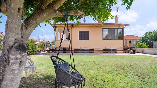 Ein Haus mit Schaukelstuhl unter einem Baum, einem umzäunten Garten und einem Gebäude mit rotem Dach.