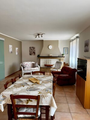 A dining area with a table set for four, a fireplace, a sofa, and a red armchair. - Lola House Between Alghero and Stintino (Palmadula)