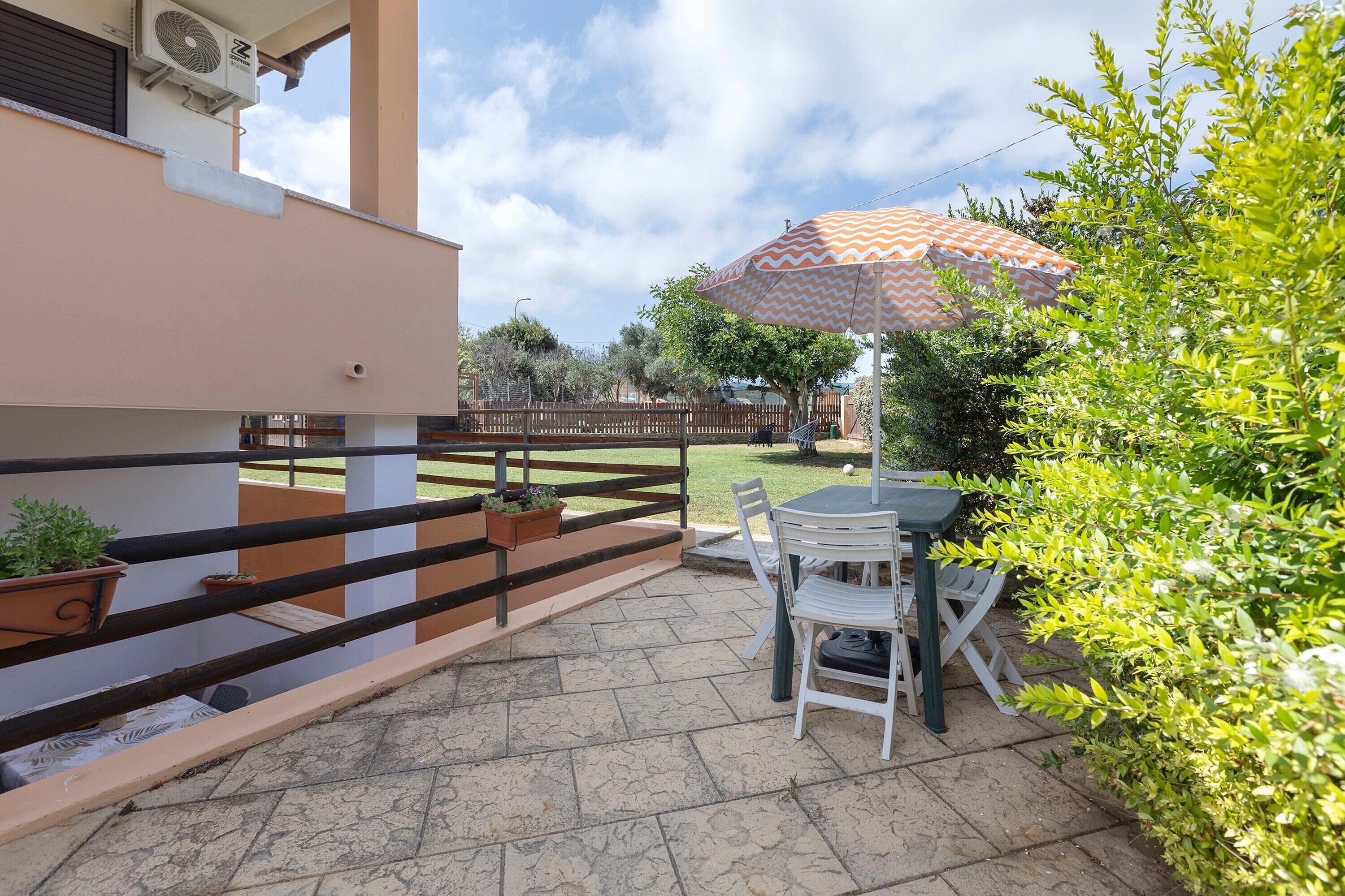 A patio with a table and chairs, a railing, and potted plants.