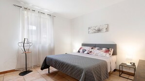 Ein Schlafzimmer mit einem Bett, einem Nachttisch mit Lampe, einer Stehlampe und einem Wandbild.