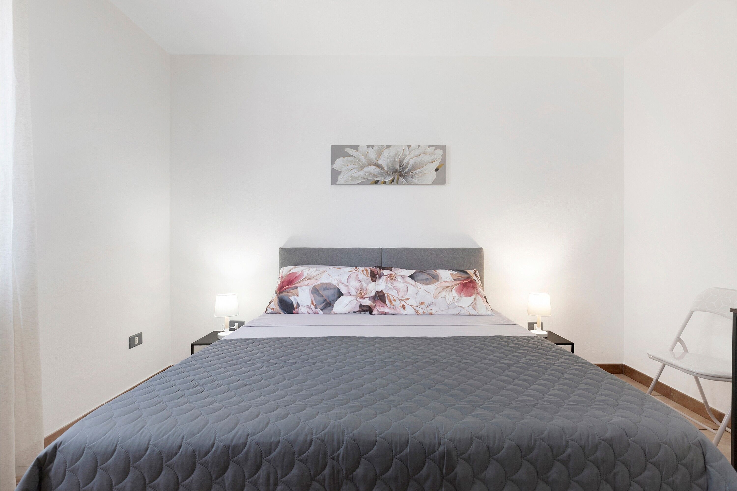 Un dormitorio con cama, almohada, una obra de arte en la pared y una mesita de noche con lámpara.