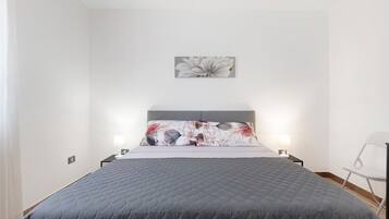 Un dormitorio con cama, almohada, una obra de arte en la pared y una mesita de noche con lámpara.