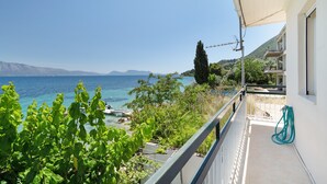 Un balcon avec vue sur la mer, un jardin et un bâtiment à la façade blanche.