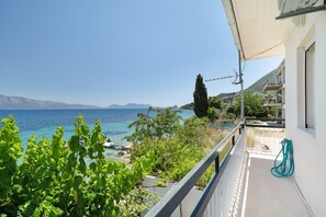 A balcony with a view of the sea, a garden area, and a building with a white exterior. - Secret Beach A Apartment with Sea View, Wi-Fi, and Air Conditioning (Nikiana)