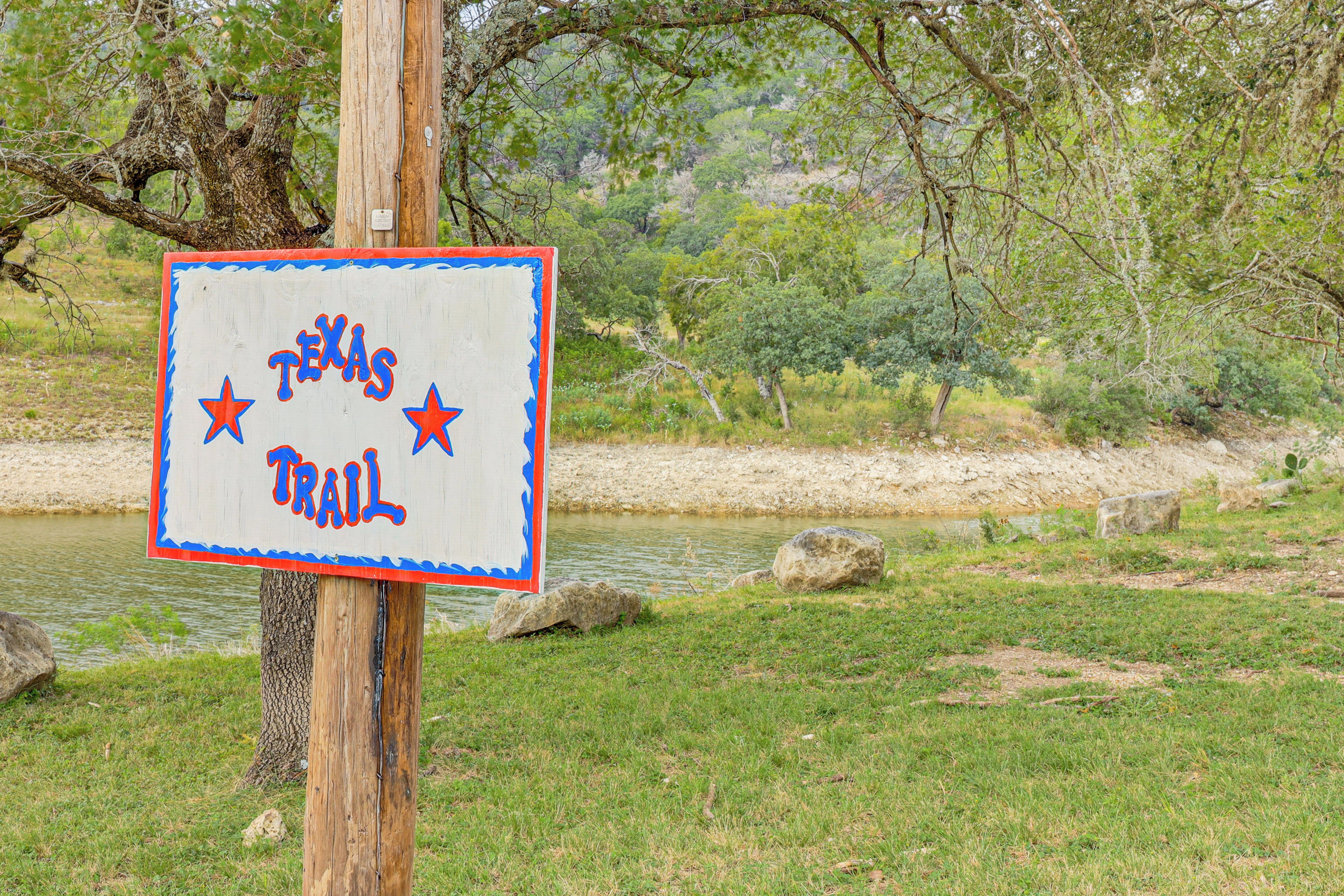 A wooden sign with 'Texas Trail' written on it, surrounded by trees and a body of water.