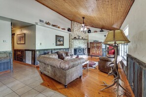 A spacious living room with a wooden ceiling, a fireplace, and a large lamp.