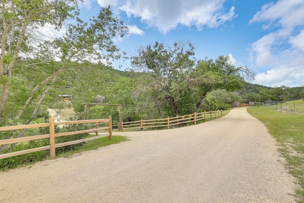 A gravel path leading to a wooden gate, surrounded by trees and a clear sky. - Horse Friendly! Hill Country Retreat w/ Views (Tarpley)